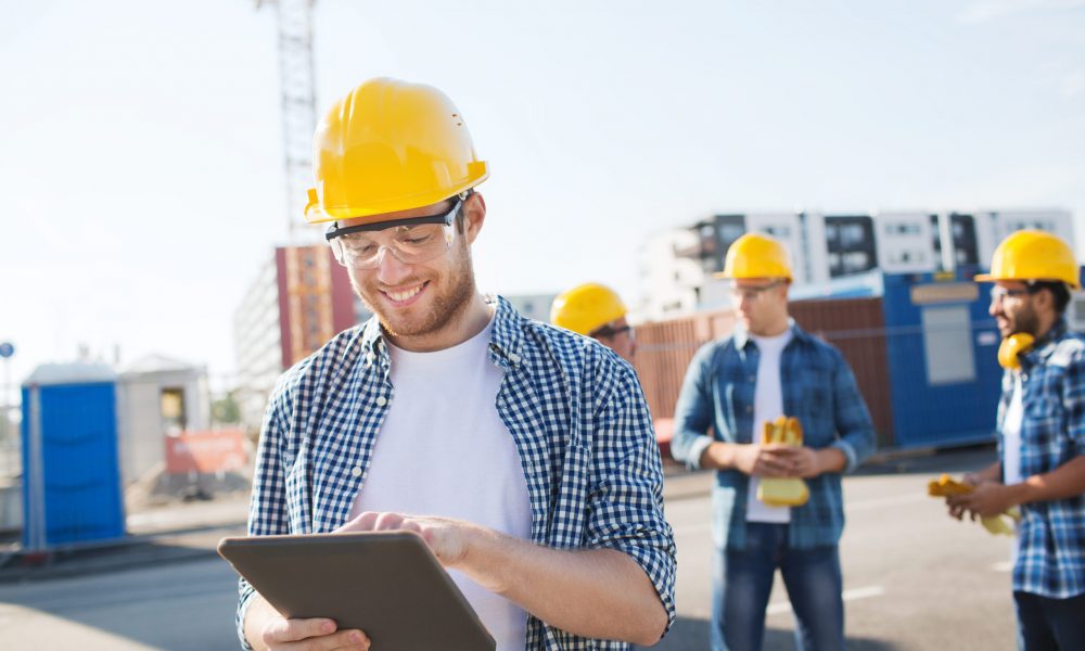 business, building, teamwork, technology and people concept - group of smiling builders in hardhats with tablet pc computer outdoors